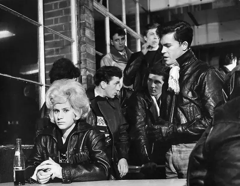 Jovens nos anos 50 usando jaquetas de couro, calças jeans e penteados rebeldes.