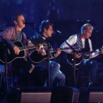 A imagem mostra a banda de rock Eagles tocando a música Hotel California ao vivo. Eles são, da esquerda para a direita, Timothy B. Schmit, Don Henley, Glenn Frey e Joe Walsh. Eles têm instrumentos musicais nas mãos. A imagem serve para ilustrar o artigo Eagles: Além de Hotel California, que fala sobre outros sucessos da banda.